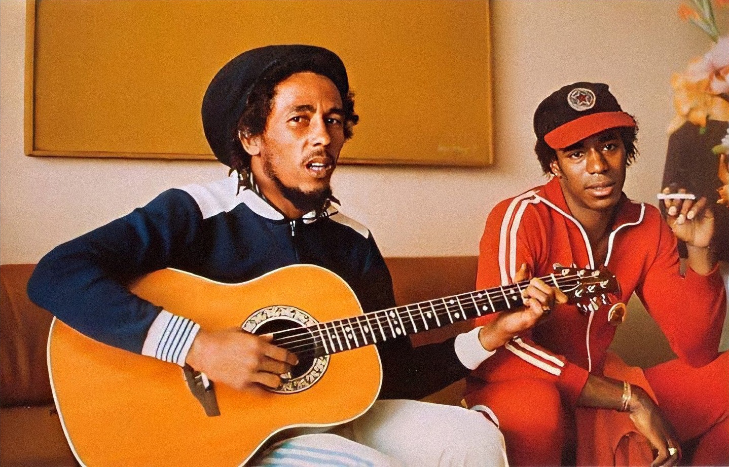 Bob Marley playing the acoustic guitar while Junior Marvin watches and smokes. Photo courtesy of Junior Marvin.